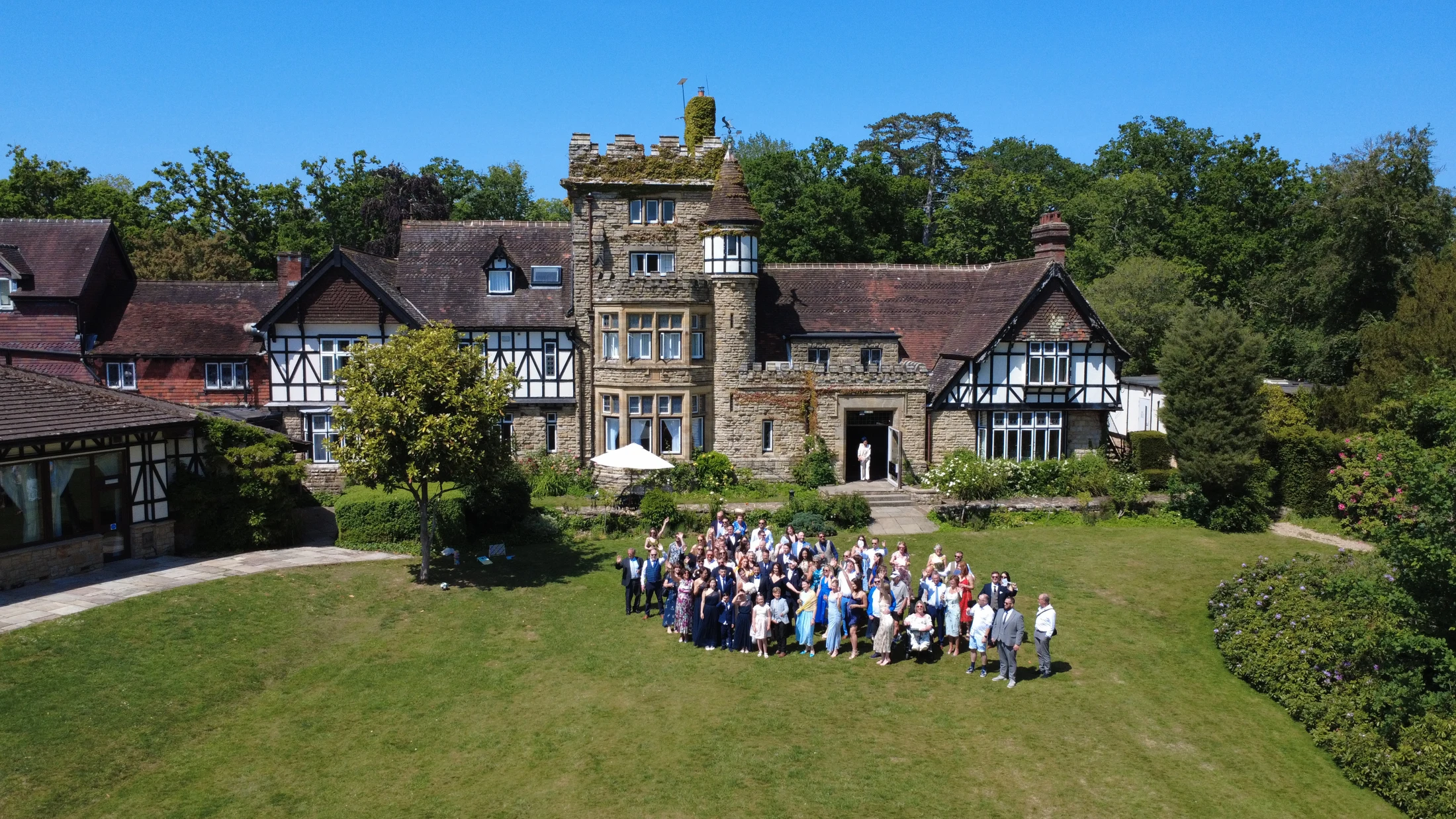 Wedding guests gathered on the lawn in front of a country house for a group photograph.