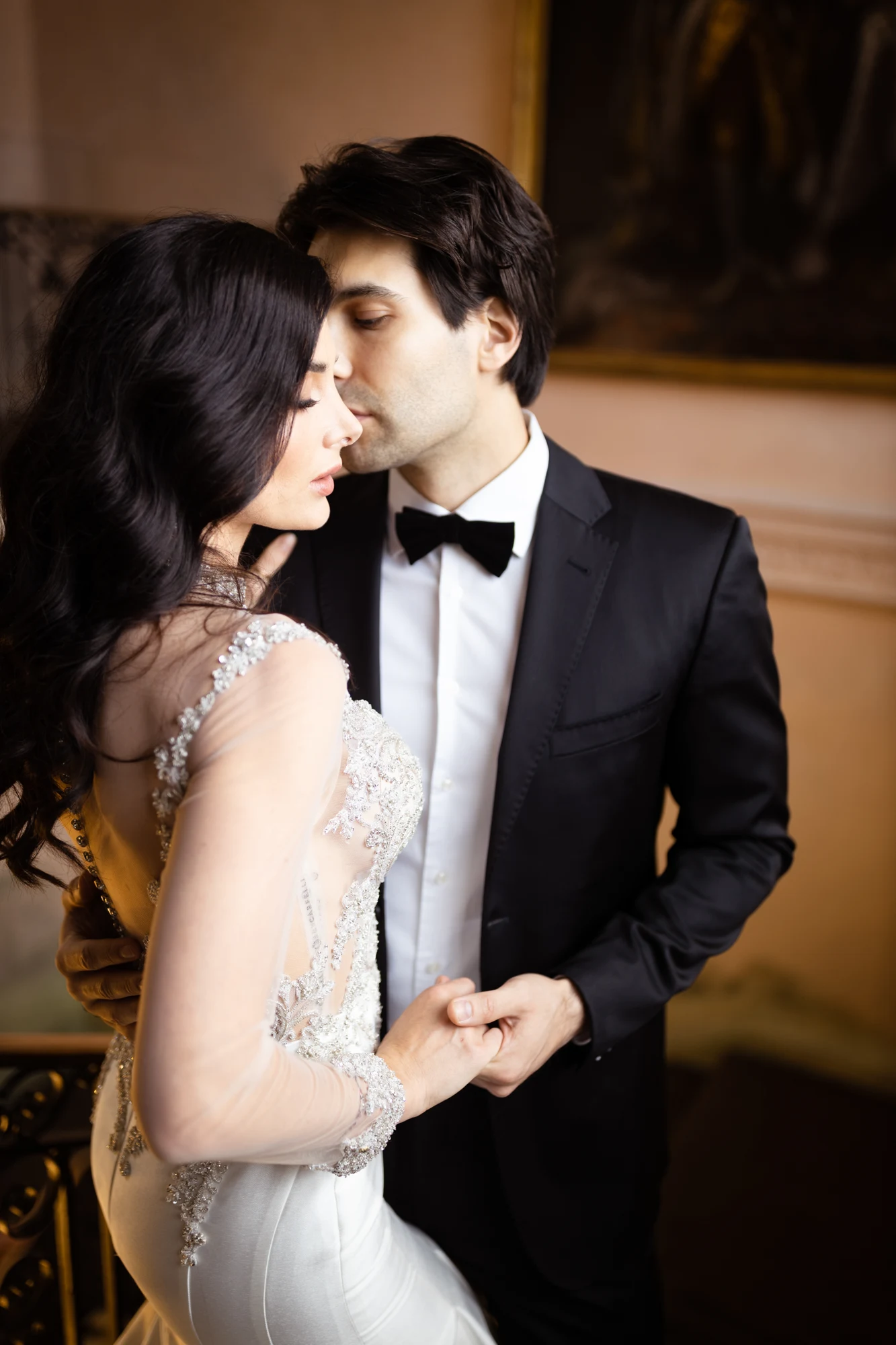 Bride and groom holding hands and leaning close together indoors.